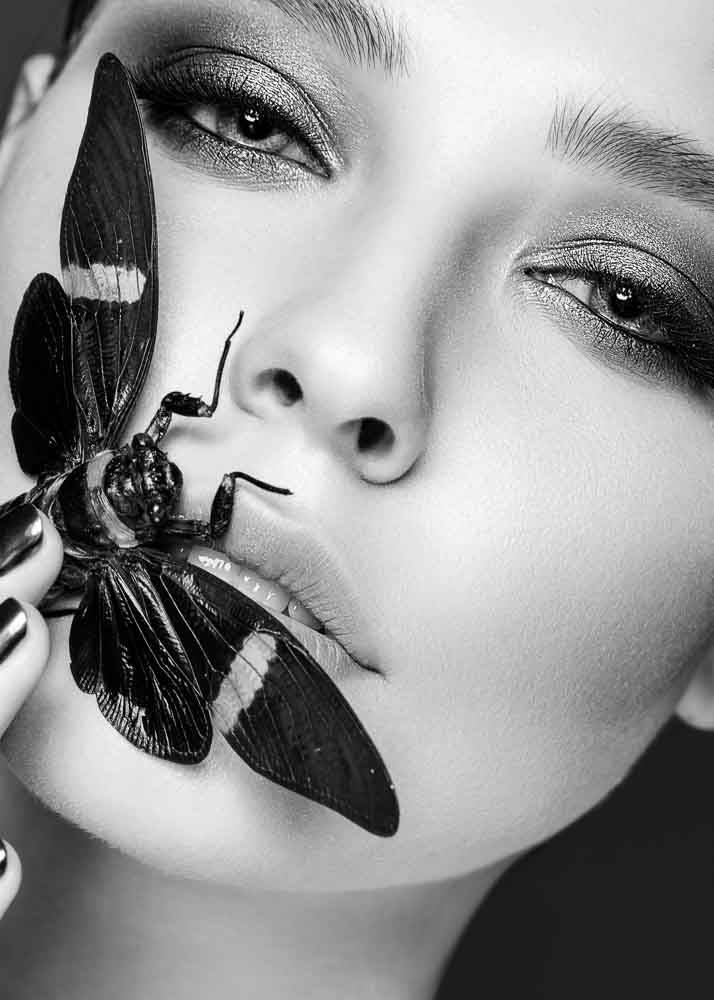 Plakat przedstawiający portret kobiety z motylem na ustach.
