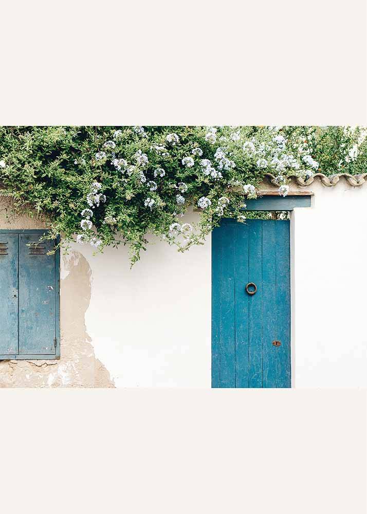 Plakat przedstawiający biały budynek z turkusowymi drzwiami oraz kwiatami.