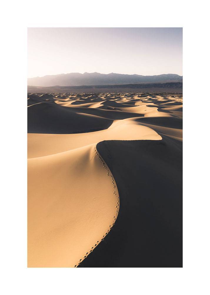 Plakat przedstawiający piaski pustyni z górami w tle.