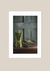 Pionowy plakat kuchenny przedstawiający zielone szparagi w kuchni na tle drewnianej ściany.