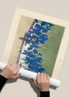 Ręce zwijające plakat przedstawiający niebieskie irysy kwitnące na łące w rulon.
